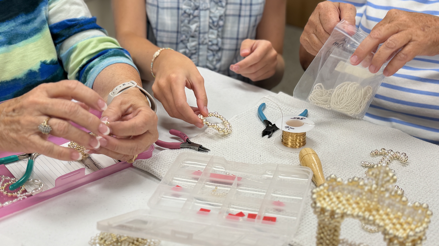 Close-up of hands creating a pearl and gold beaded cross during a senior arts and crafts session.
