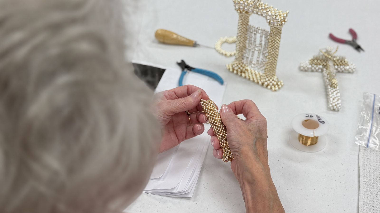 Close-up of seniors creating beaded jewelry during a craft workshop using beads, wire, and jewelry tools.
